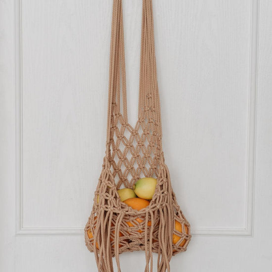 resuable mesh bag with fruit hanging on door. Representing how to zero waste shop for food