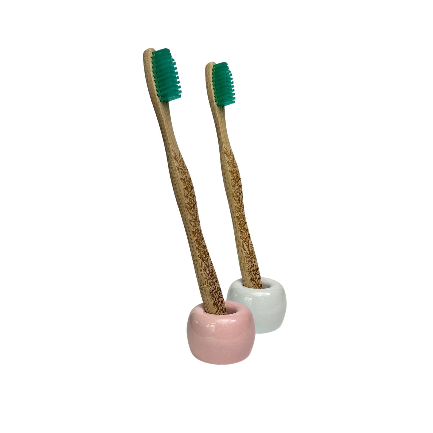 2 small ceramic toothbrush holder in glossy white and a pink finish holding a bamboo toothbrush