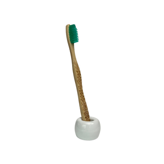 small ceramic toothbrush holder in glossy white finish holding a bamboo toothbrush